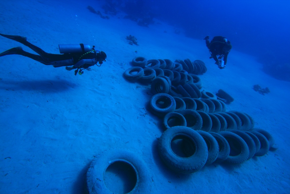 Clean up of environmental pollution problem. Scuba divers remove car tyres from ocean reef