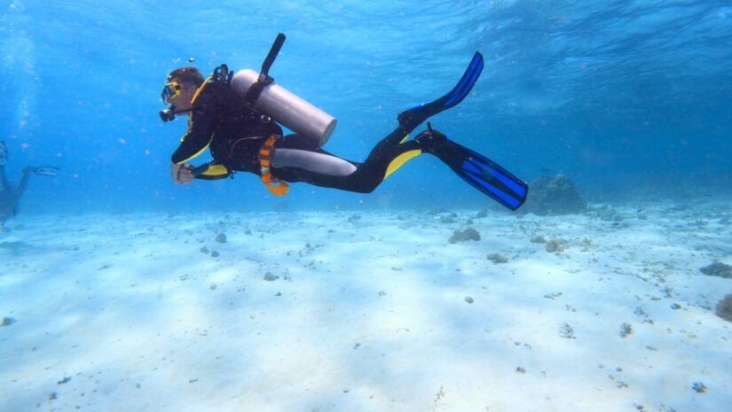 Scuba diver with fins swimming near the bottom of the ocean