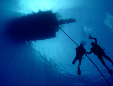 scuba divers ascending descending on the line of boat rope under