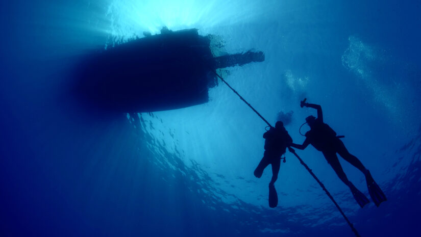 scuba divers ascending descending on the line of boat rope under