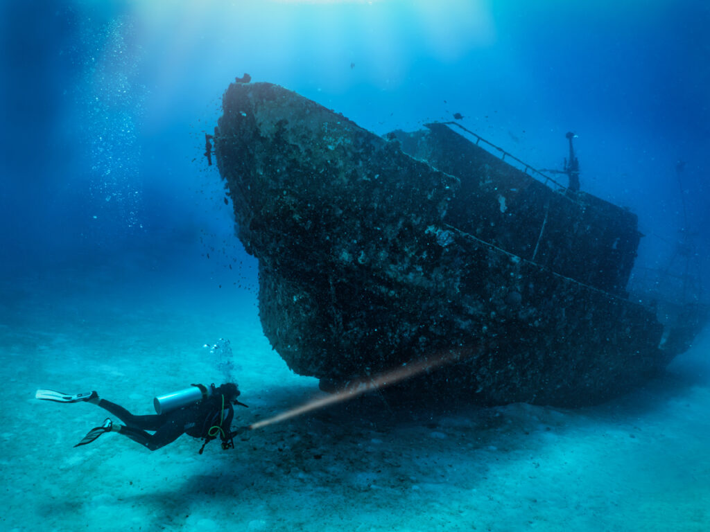 A scuba diver with a torch explores a sunken shipwreck at the se