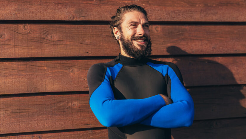 Male surfer lifestyle portrait. Man in wetsuit with bodyboard surfing equipment