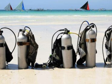 scuba tanks and BCDs lined up on the beach