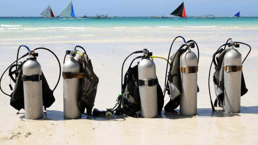 scuba tanks and BCDs lined up on the beach