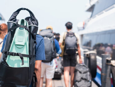 Traveler man with diving fins and travel bag walking the boat