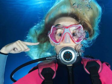 scuba diver pointing at her right ear