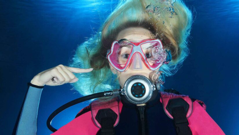 scuba diver pointing at her right ear