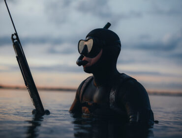 Man spearfishing with a speargun in the middle of the sea. Adventurous fisherman hunting for fish while wearing a scuba mask and a wetsuit