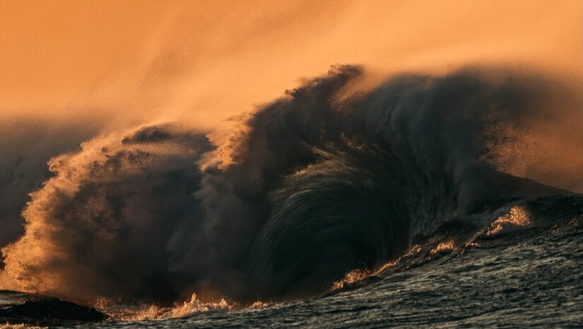 a huge wave over the sea during sunset