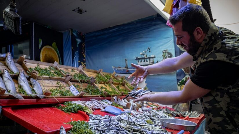 white man holds up fish at a market