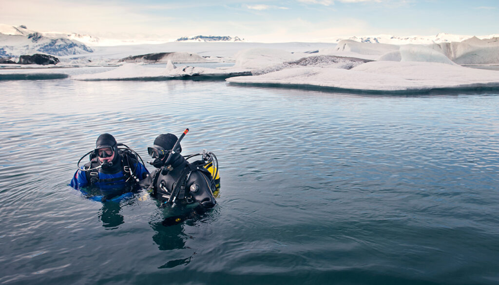 Scuba divers in sea with snow covered landscape in background by Cavan for Adobe