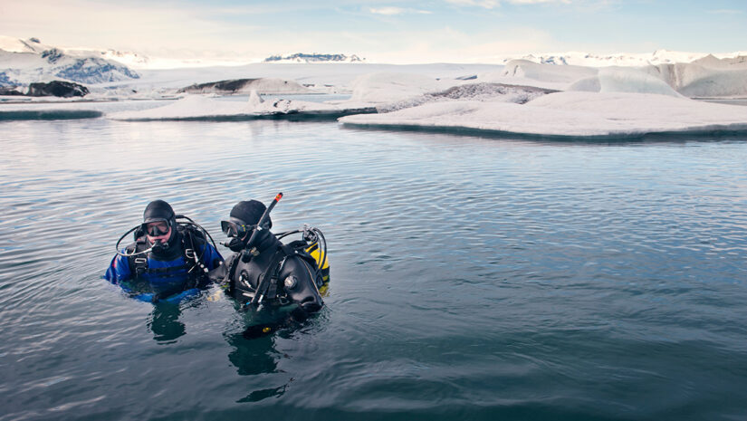 Scuba divers in sea with snow covered landscape in background by Cavan for Adobe