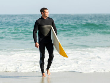 male surfer in full body wetsuit by the shore
