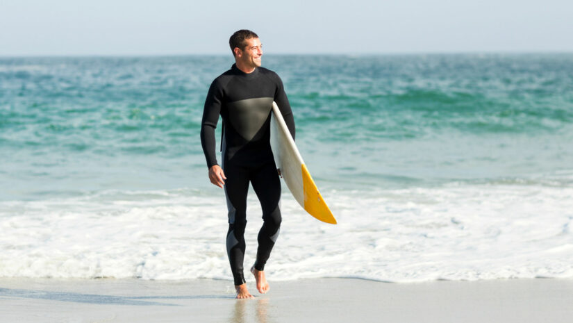 male surfer in full body wetsuit by the shore