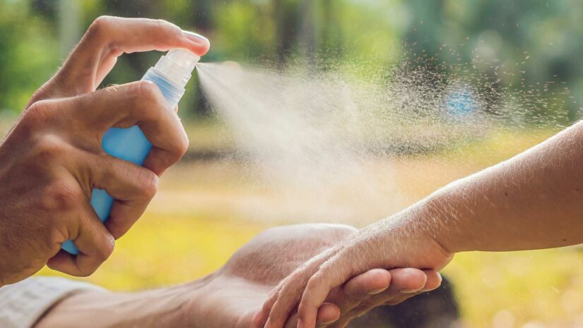 spraying insect repellent on a child’s arm