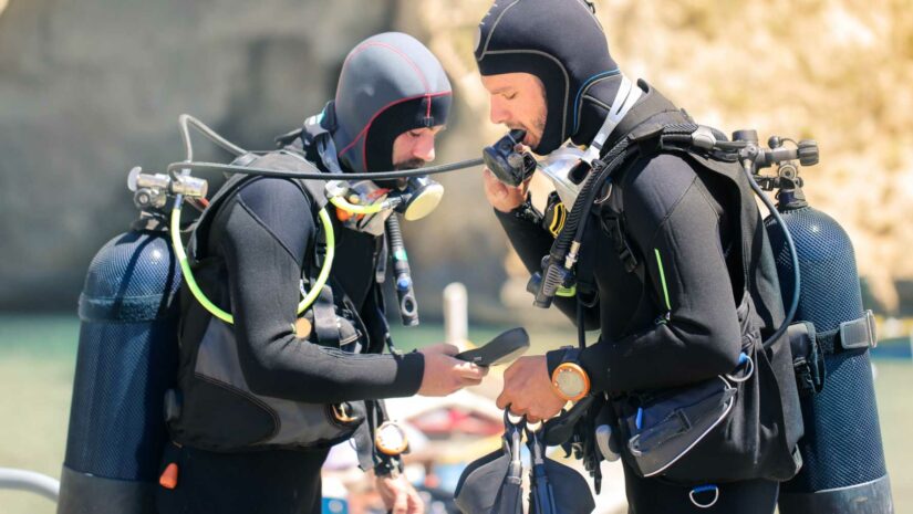 two divers in wetsuits checking their dive gear