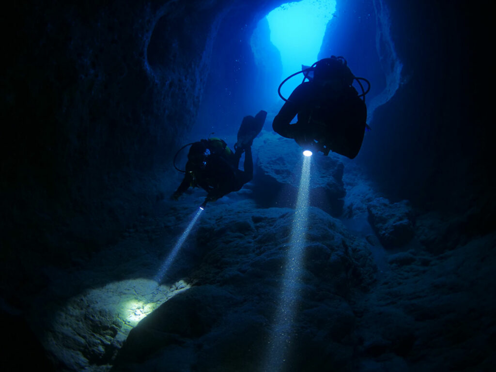 two scuba divers with dive light in cave