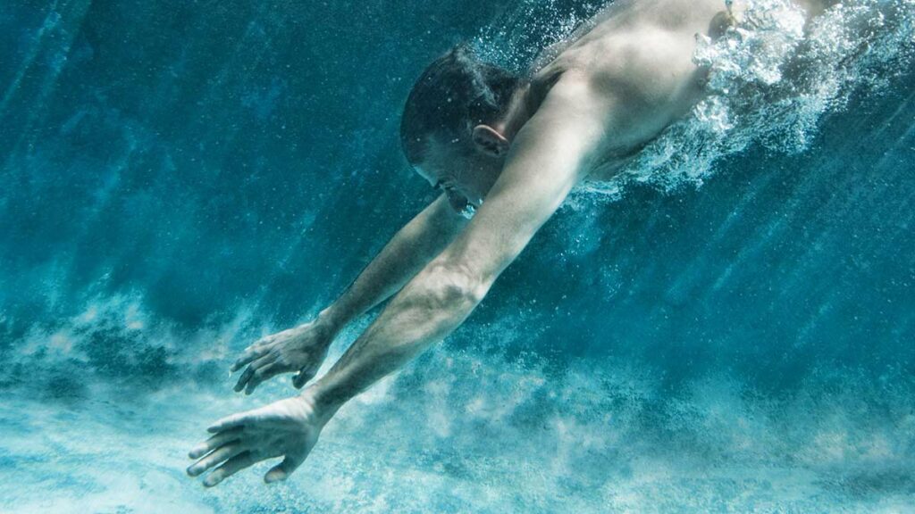 man diving underwater with open eyes
