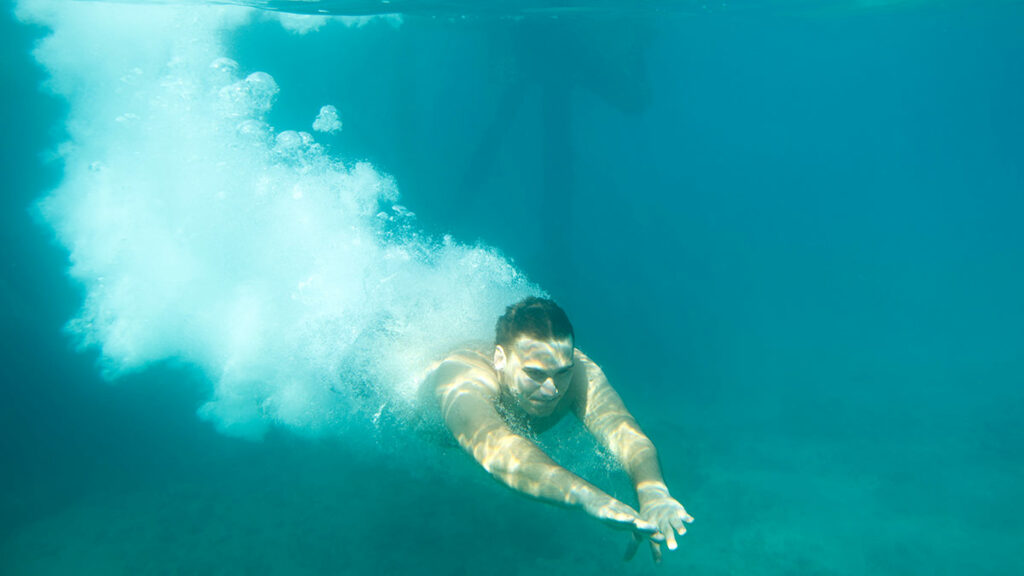 man diving underwater with open eyes