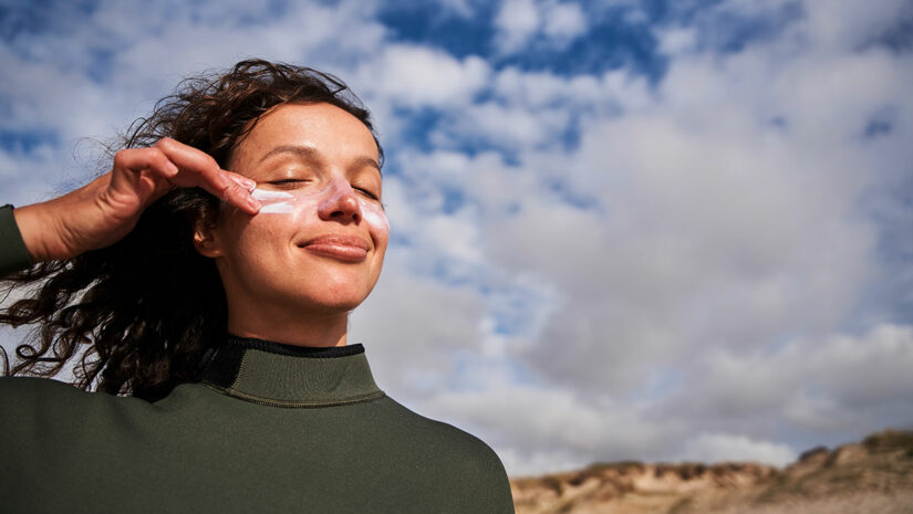 woman outdoors wearing wetsuit and applying sun screen on cheeks