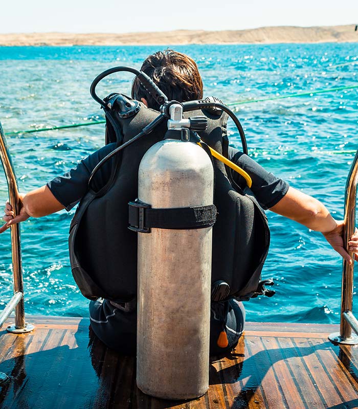 person with scuba diving tank and equipment sitting on pier ready to dive