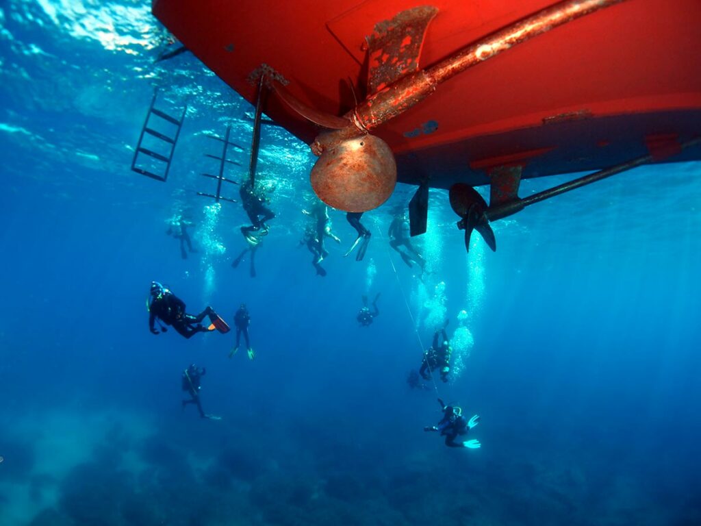 group of scuba divers performing safety stop under boat while diving underwater