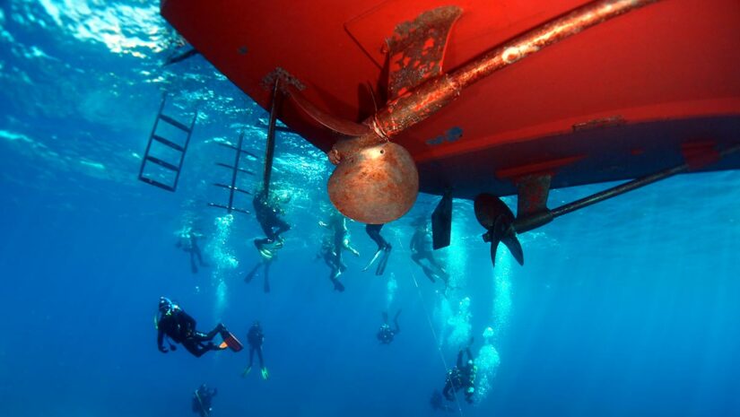 group of scuba divers performing safety stop under boat while diving underwater