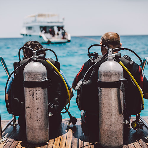 scuba divers with gear sitting on pier overlooking boat