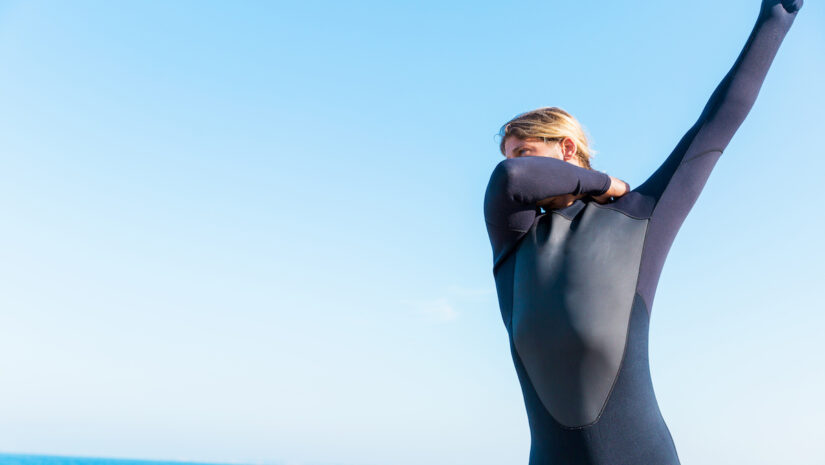 A young surfer putting on his wetsuit on the beach