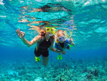 Happy family - mother, kid in snorkeling mask dive underwater with tropical fishes in coral reef sea pool. Show by hands divers sign OK. Travel lifestyle, beach adventure on summer holiday with child