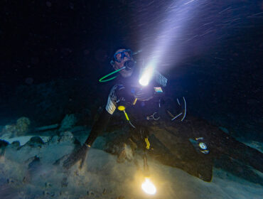 diver in strong current at night with torch via adobe stock