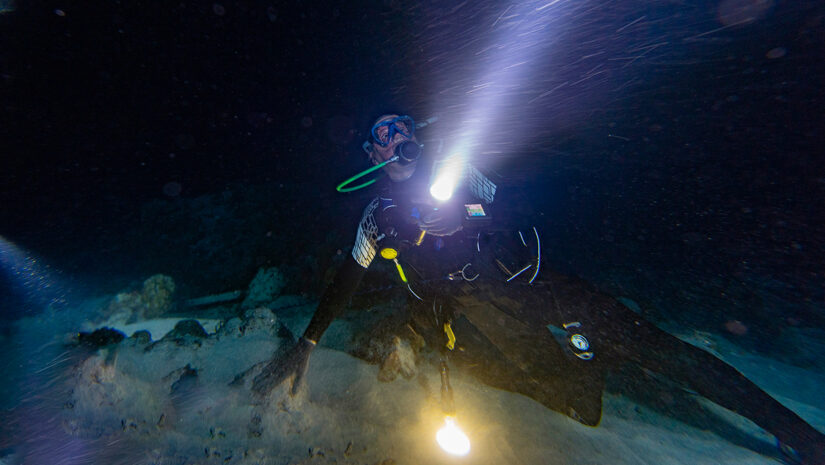 diver in strong current at night with torch via adobe stock