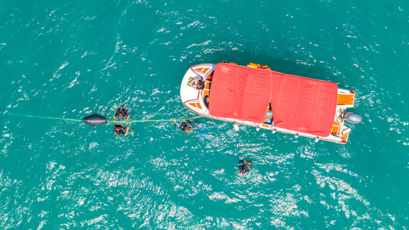 Boat with people diving suit mask and fins in the sea arrived in the lagoon to dive to the bottom, aerial top view