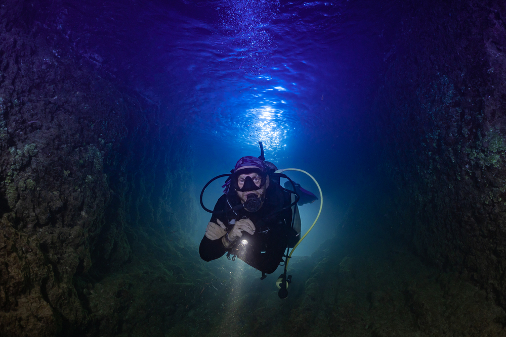 A man scuba diving at night deep in the ocean.