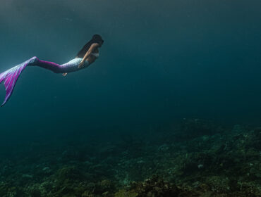 Young female free diver swims underwater in a colorful and sexy mermaid costume.