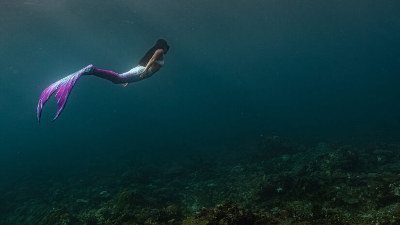 Young female free diver swims underwater in a colorful and sexy mermaid costume.
