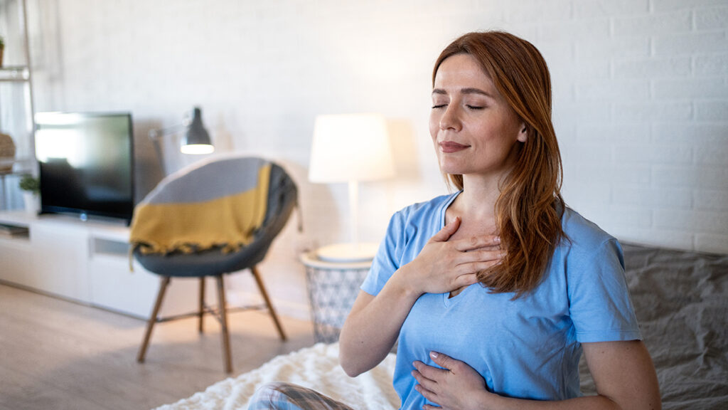 Peaceful woman meditating in her bedroom, enjoying a moment of mindfulness and self-care through a deep breathing exercise, promoting relaxation and inner peace