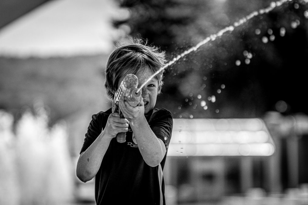 black and white photography of kid playing with a water gun