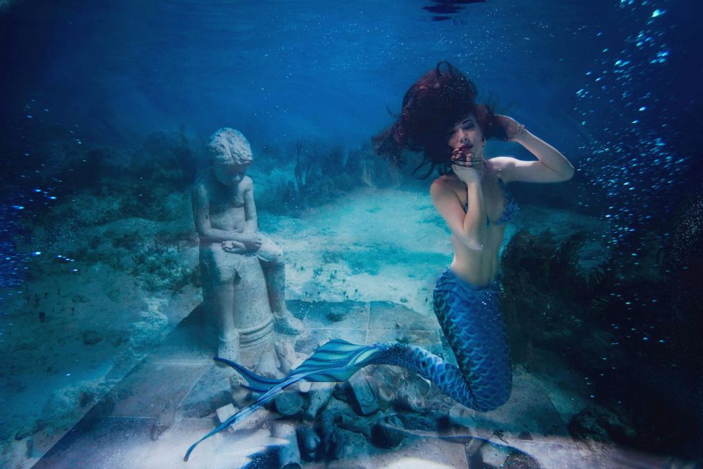 gorgeous mermaid posing for camera in front of an underwater statue