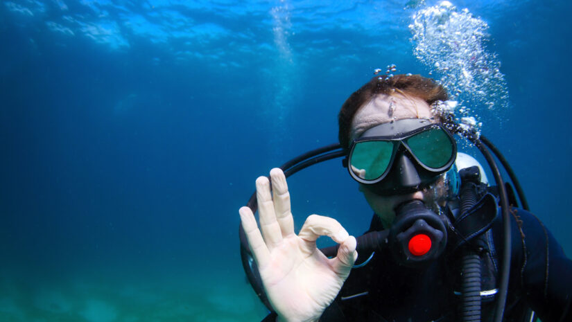 Underwater shoot of a man diving with scuba and showing ok signal