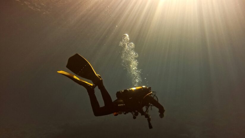 man drift diving with the sun shining through the surface