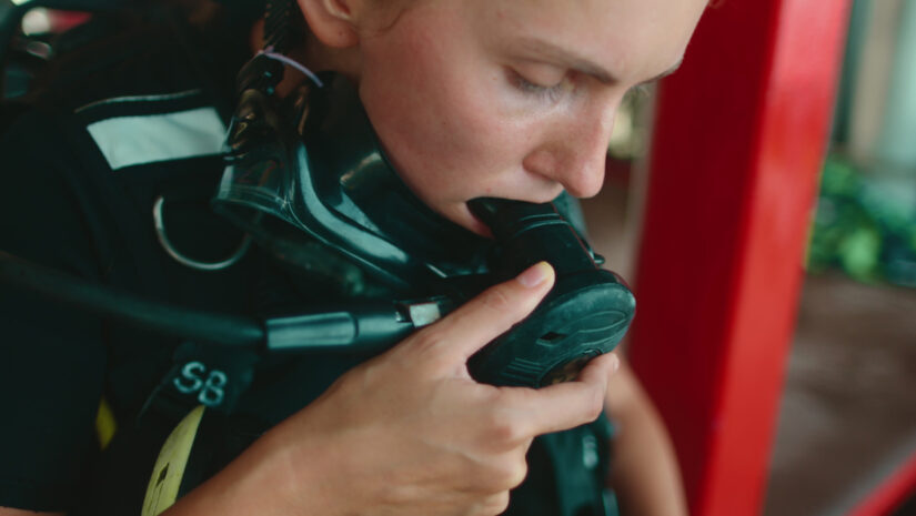 Young scuba diver in thailand prepares to dive into clear waters, checking equipment with focus. Surrounding sea colors are vibrant as she breathes deeply for an underwater adventure