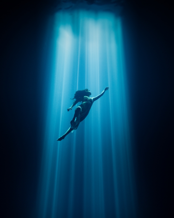 underwater diver poses under a beam of light from the surface