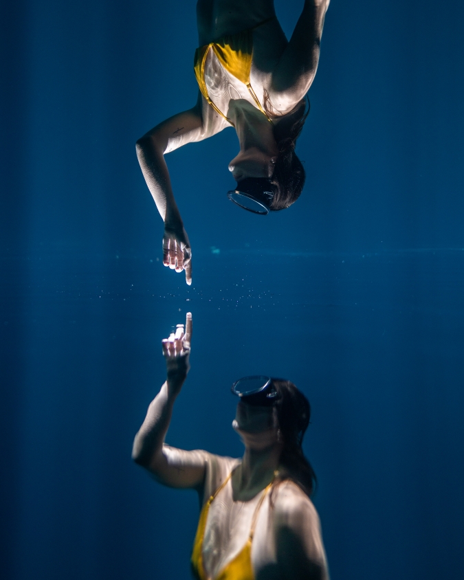 underwater photography example of mirrored underwater model touches her finger on the surface