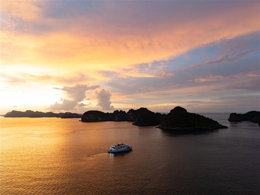 boat cruises towards an island in the sunset