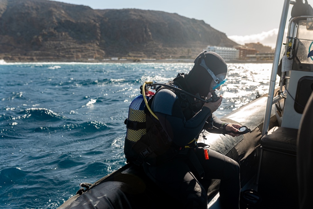 Professional scuba diver preparing for diving, adjusting equipment and checking compass on inflatable boat 
