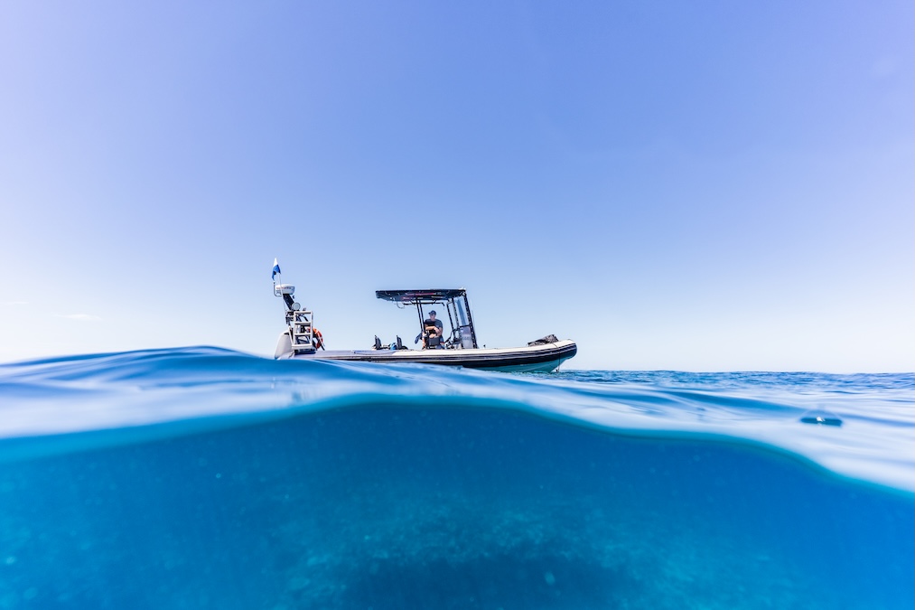 A split-level photograph showing scuba divers on a boat above the water's surface, and the ocean view below