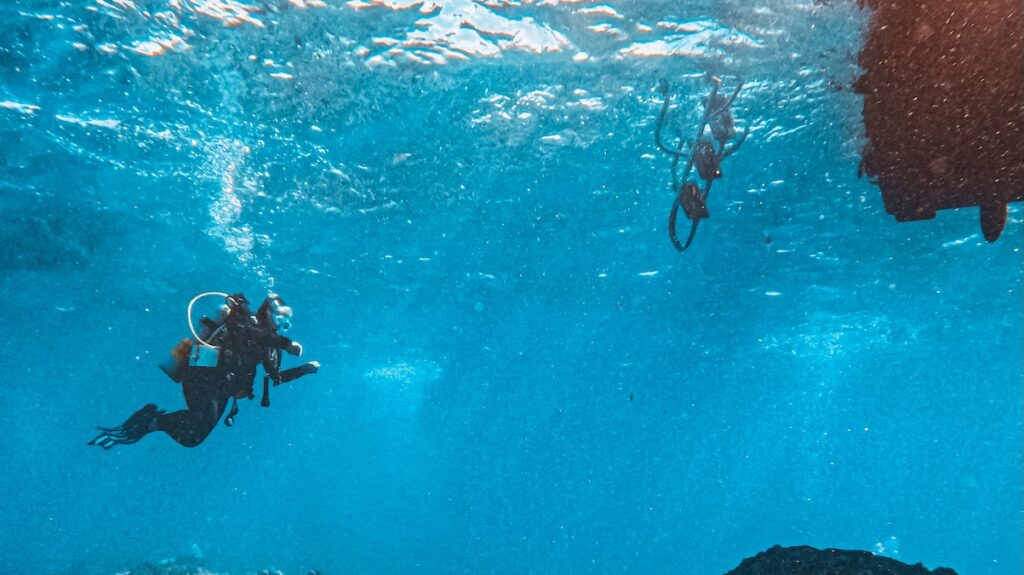 A scuba diver exploring clear blue water, positioned on the left side of the frame