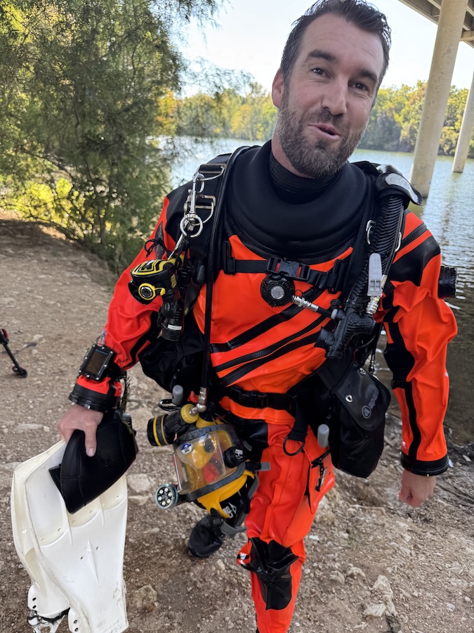 Austin PD diver fully equipped in a high-visibility orange drysuit holding swim fins near a body of water